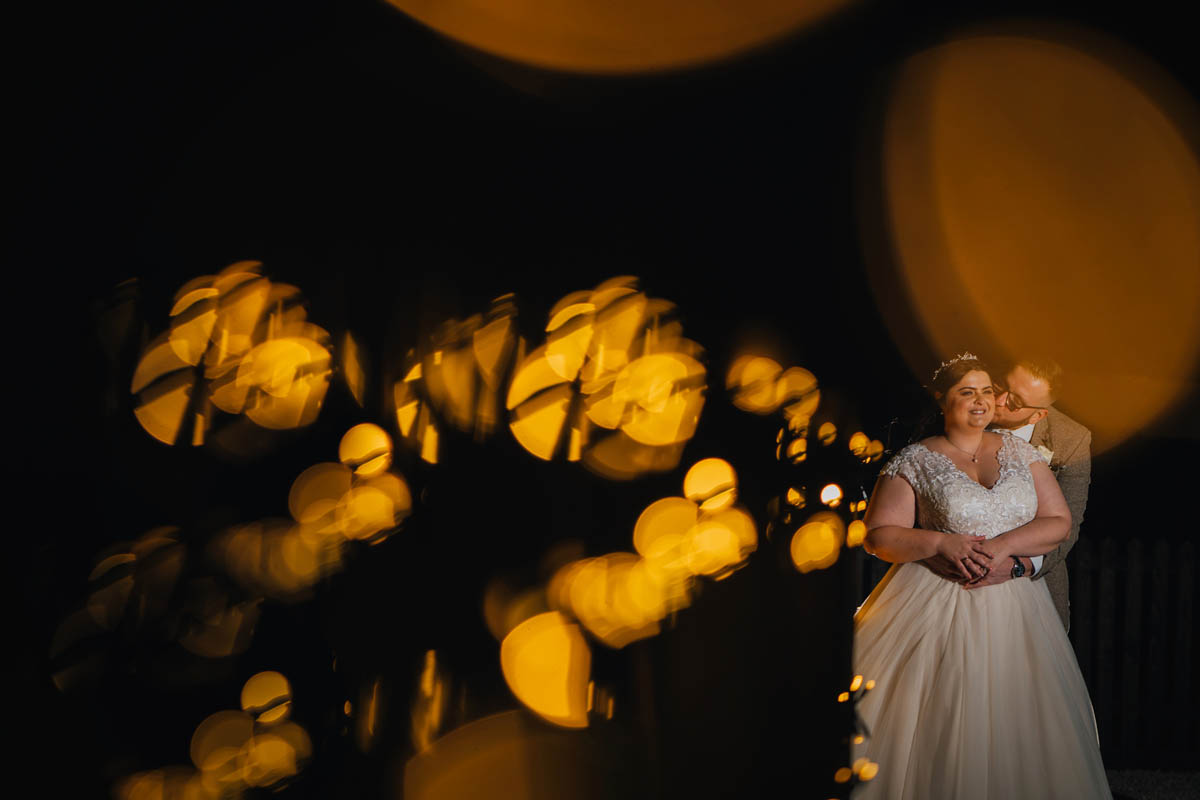 fairy lights create bokeh and the bride and groom post towards the back of the image, they are lit by an off camera flash