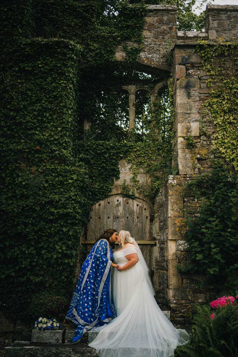 two brides kiss under an old archway at Thornbury Castle, Bristol