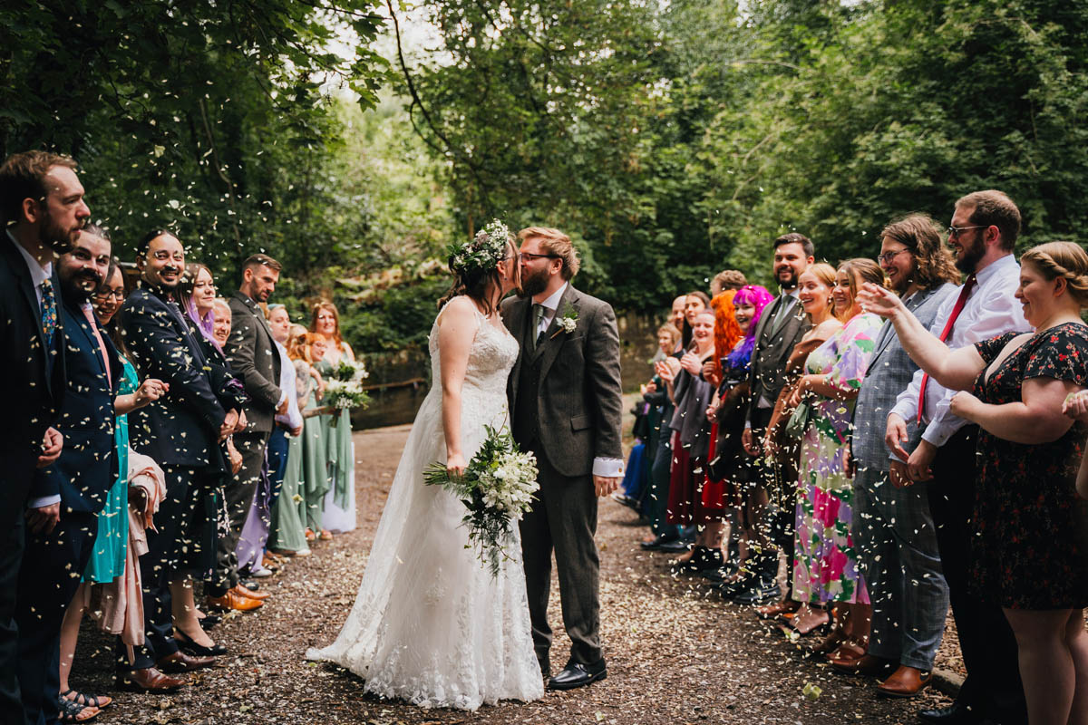 the couple kiss as their wedding guests shower them in confetti