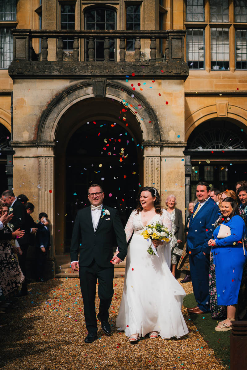 the bride and groom look jubilant as guests shower them in confetti