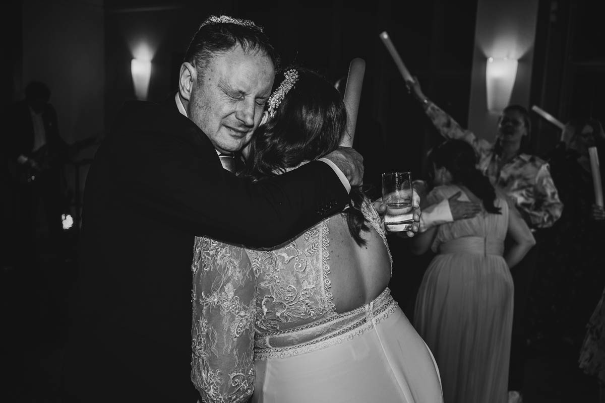 the father of the bride's hugs his daughter emotional on the dance floor at her wedding - in black and white