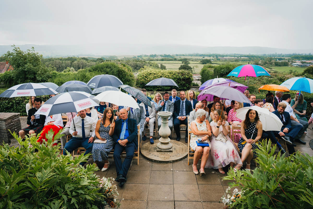wedding guests sit in the garden at Barley wood under umbrellas