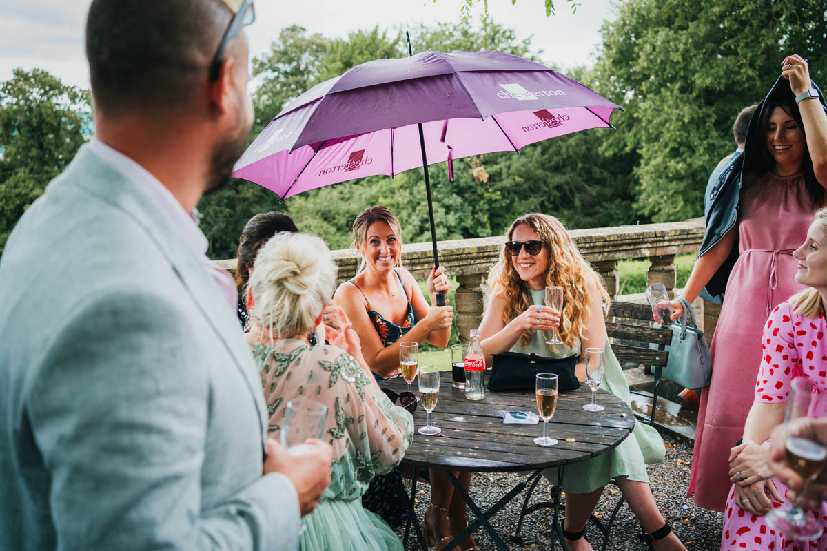 wedding guests drink champagne under umbrellas as it rains
