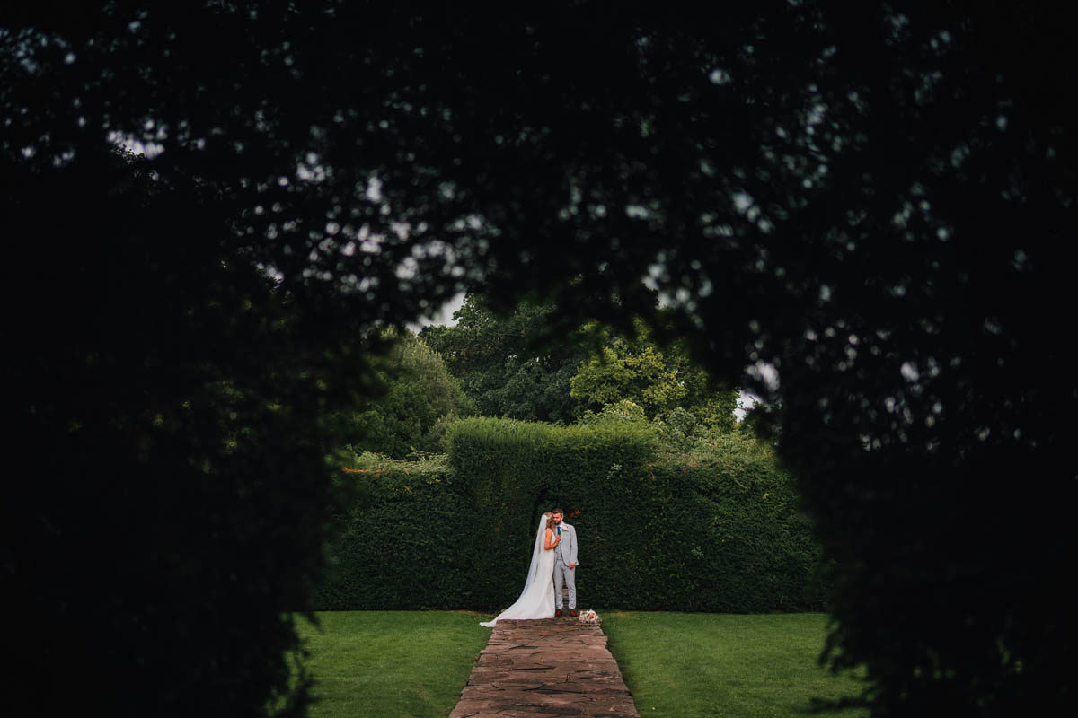the bride and groom framed by the hedges in barley wood gardens