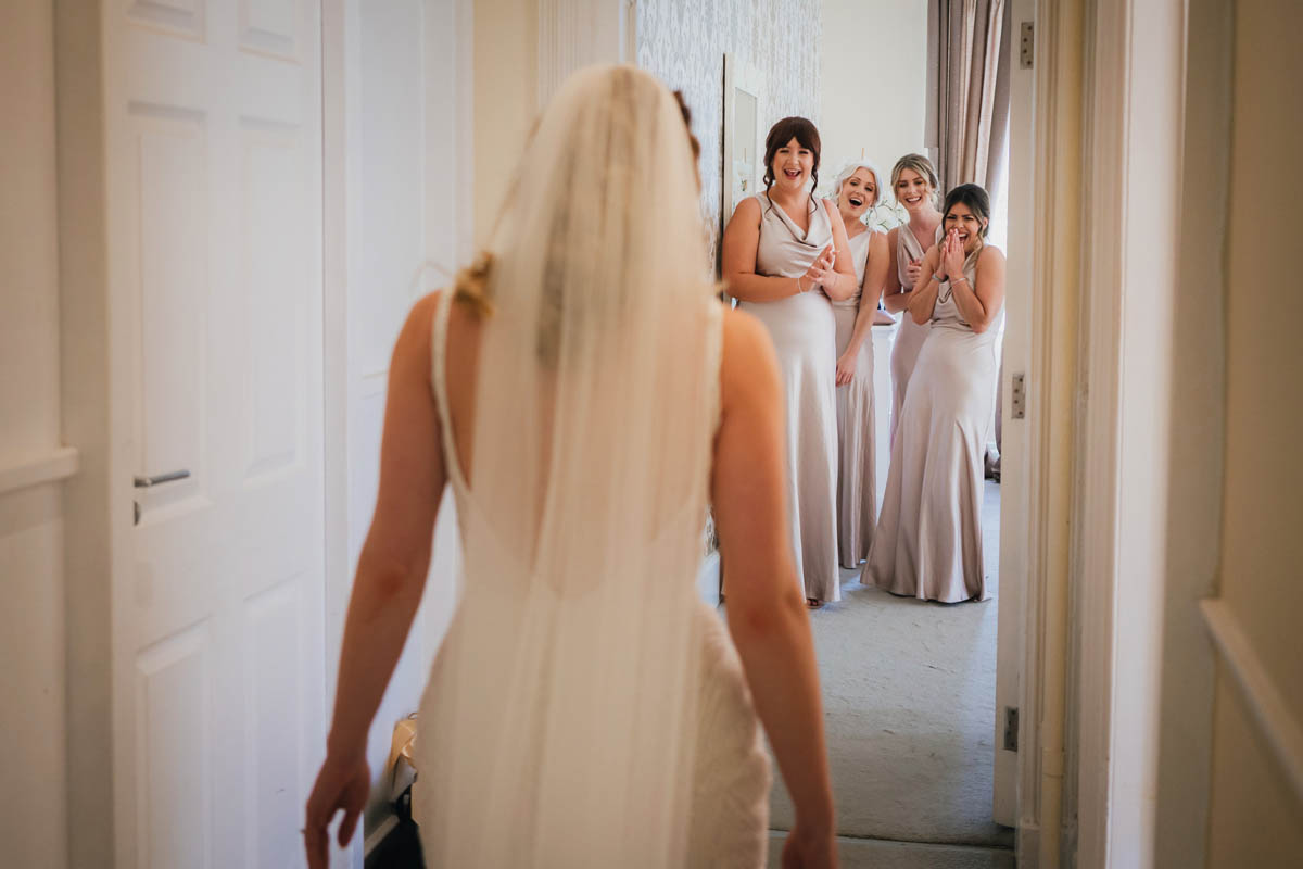 the bridesmaids look excitedly at the bride in her wedding dress
