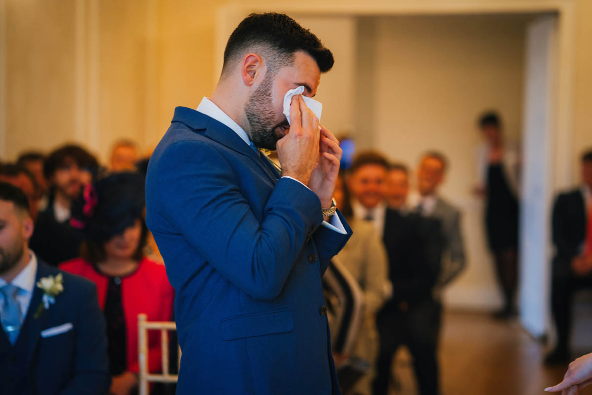 the groom using a tissue to wipe away a tear