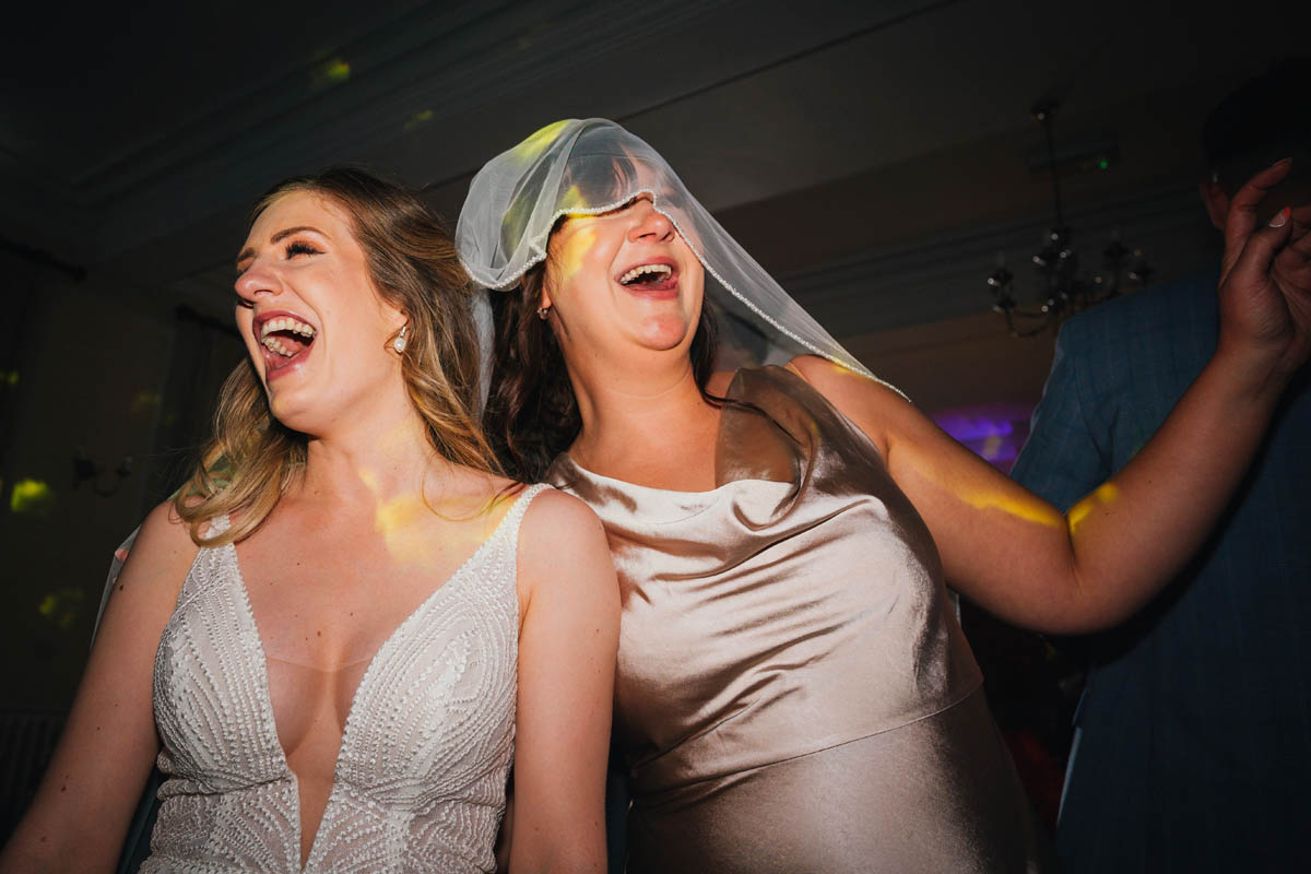 the bride and her bridesmaid on the dance floor, sharing the bride's veil