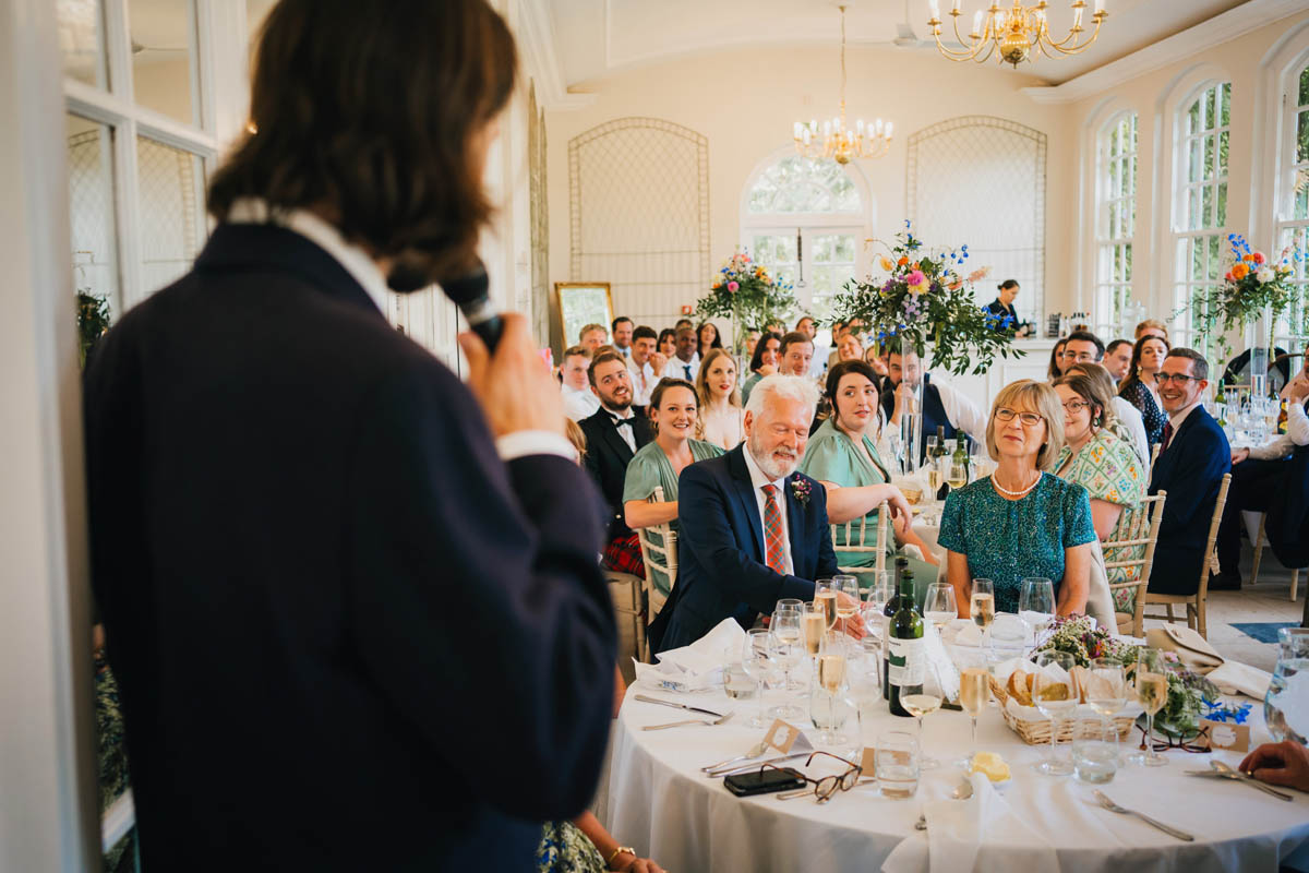 wedding guests laugh at the best man's speech in the orangery