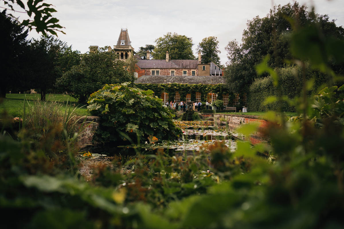the ornamental canal with the orangery at Goldney hall behind in summer and full of foliage and greenery, wedding guests can be seen in the distance