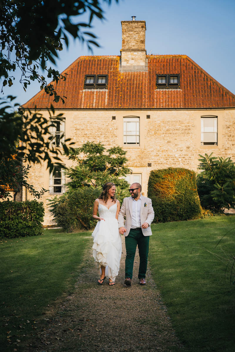 the newly-weds walk down the path in front of the farm buildings at folly farm