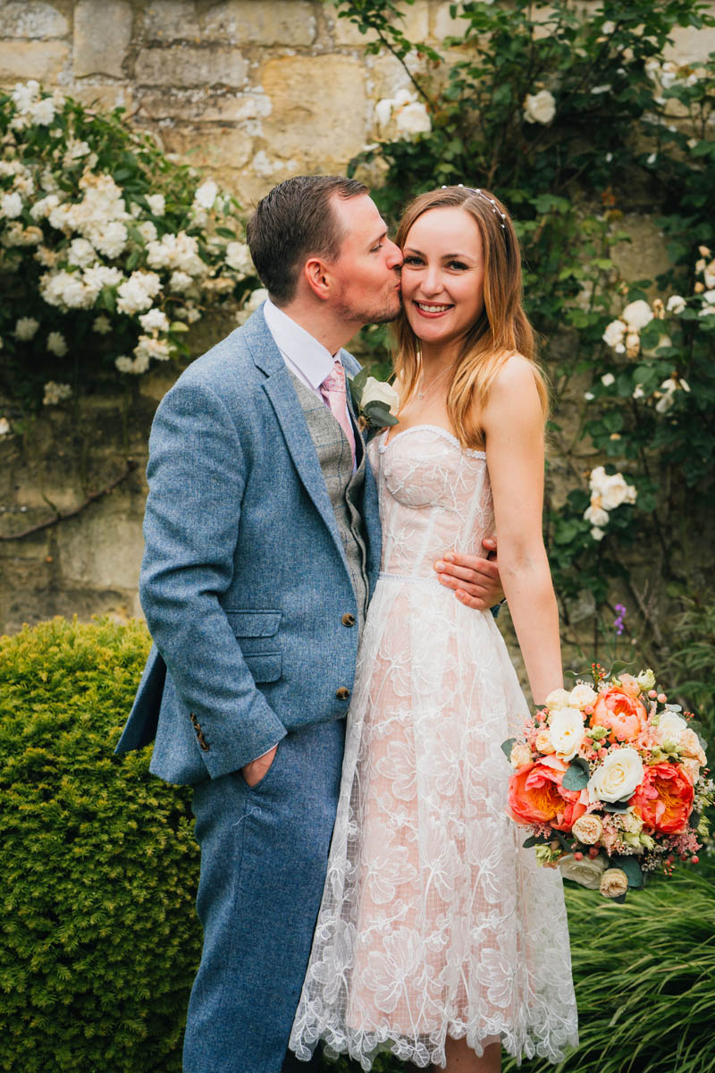 the groom kisses his new wife as she smiles at the camera