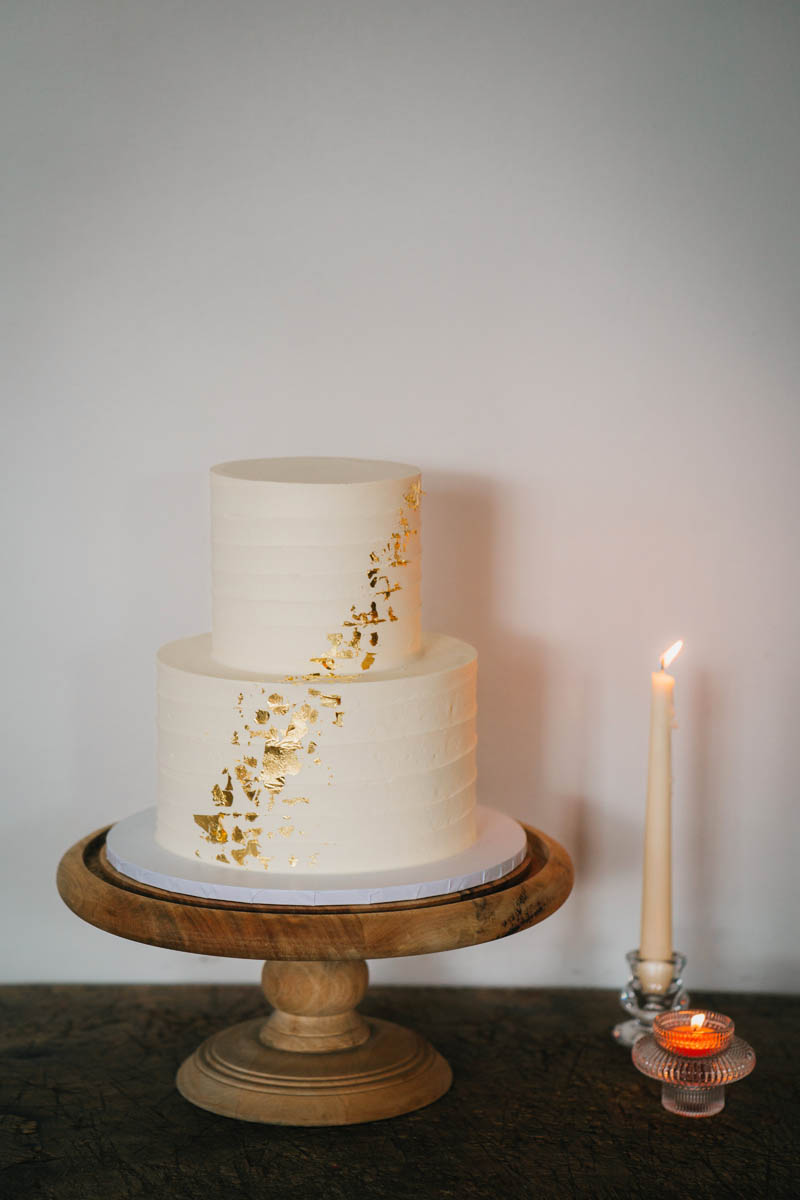 a two tiered simple ivory wedding cake next to a lit candle