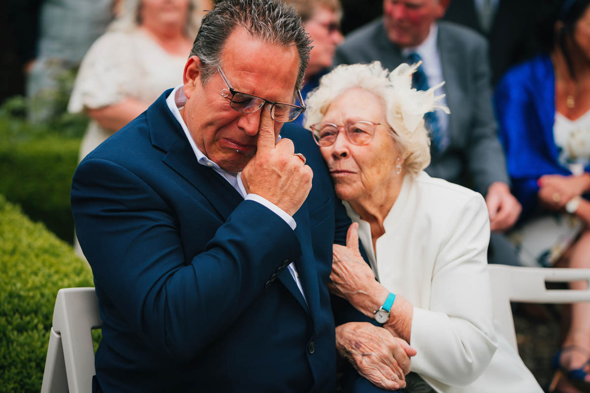 the father of the groom is comforted by his mum as he sheds a tear at the wedding ceremony