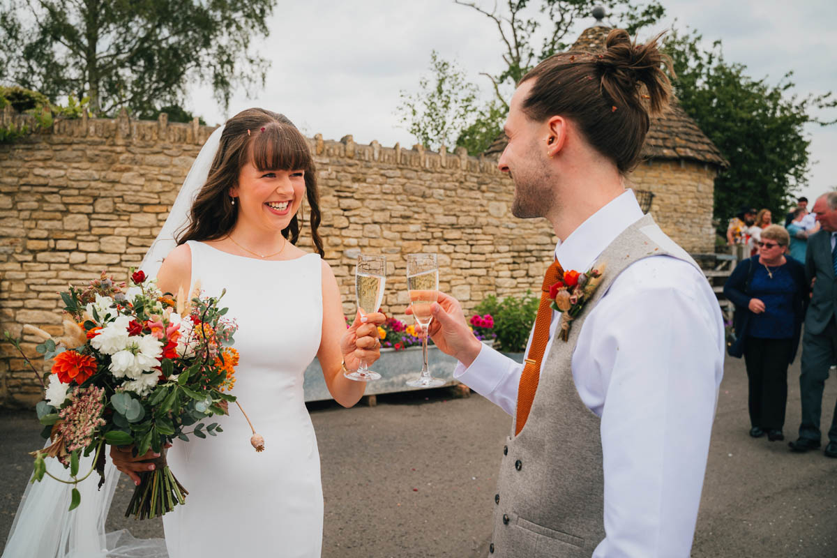 the bride and groom grin at each other and clink champagne glasses