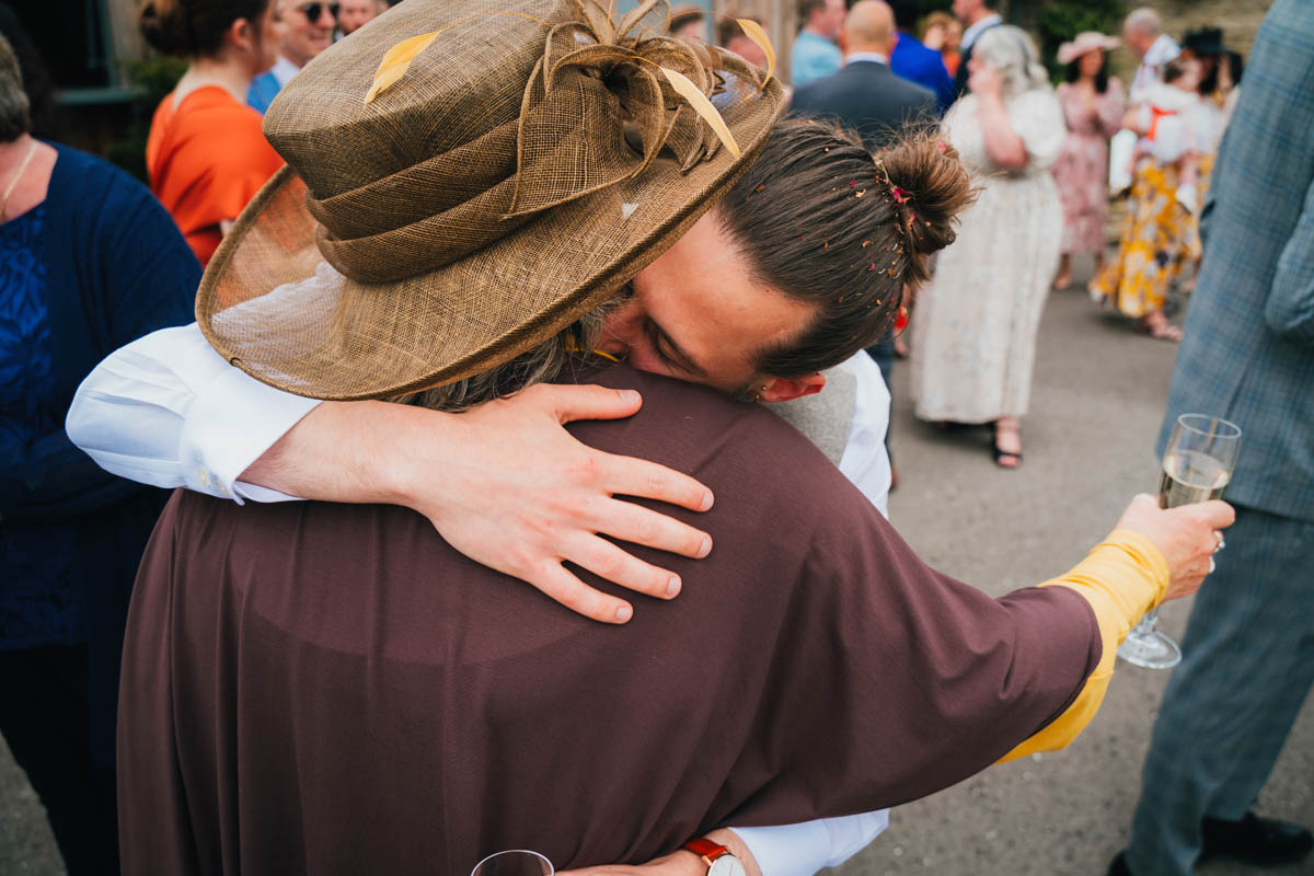 the groom hugs his mum as she holds a glass of champagne