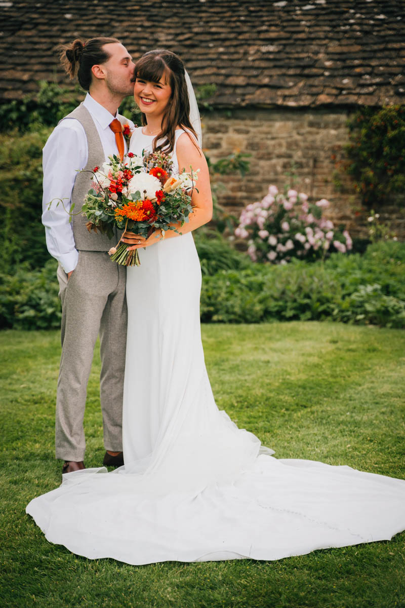 the groom kisses his new wife in front of a pretty stone wall