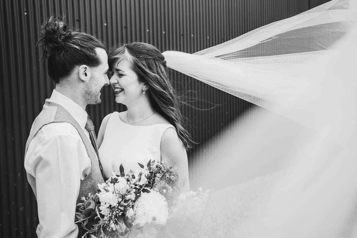 the bride's veil gets caught in the veil as the bride and groom rest foreheads together and smile