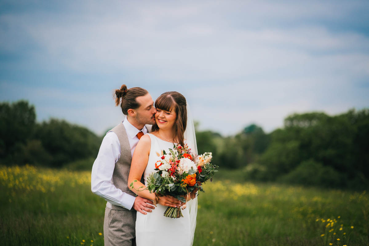 the groom kisses his new wife. She holds a bridal bouquet