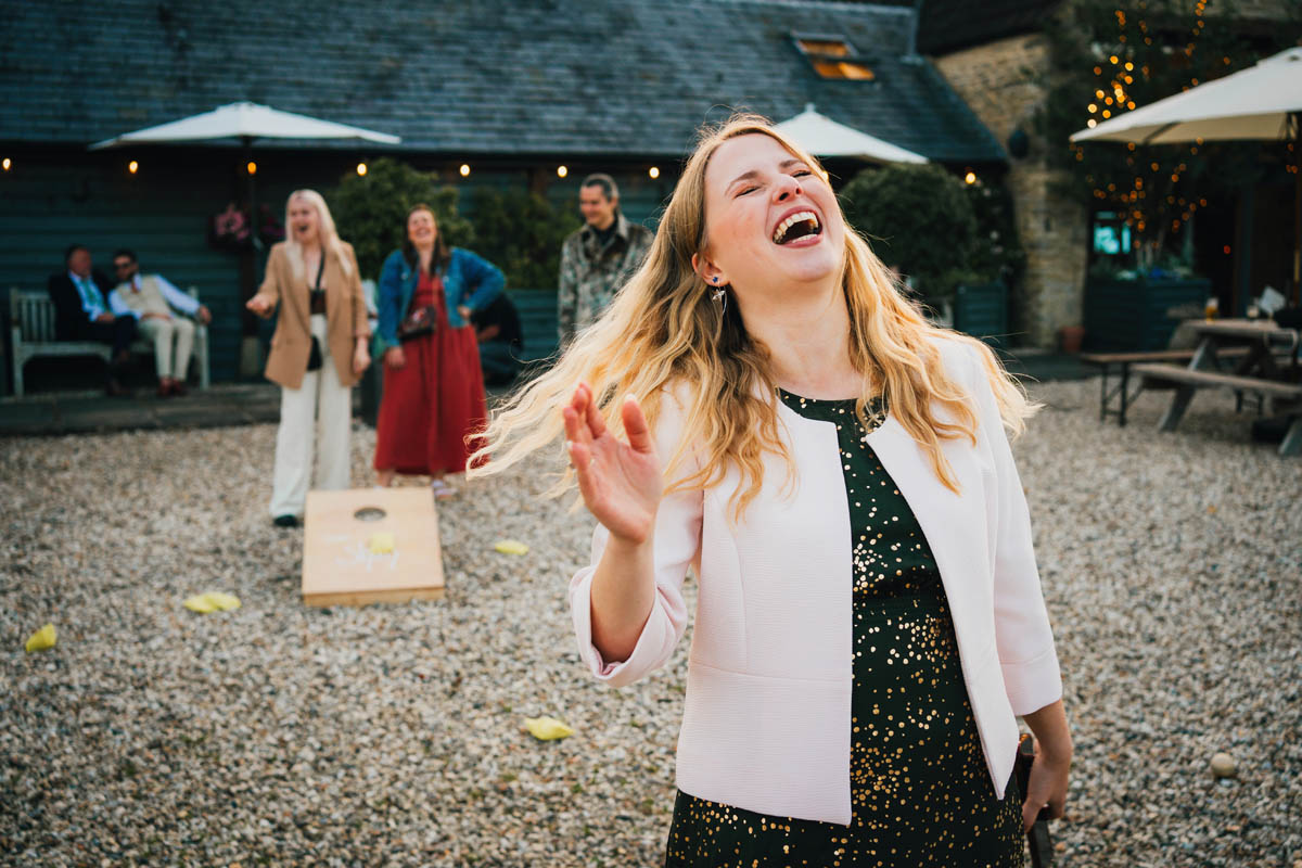 a wedding guests laughs as she throws a beanbag