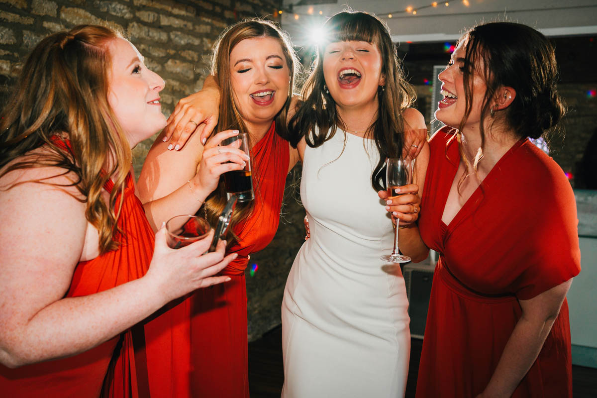 the bride hugs her three bridesmaids as they sing on the dance floor