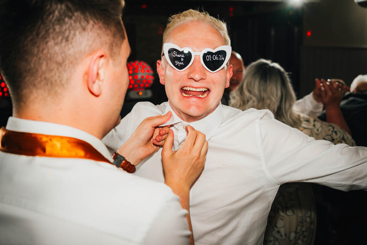 a groomsman unbuttons another groomsman