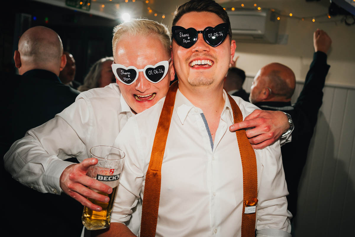 two groomsmen pose for the camera while drinking beer on the dance floor