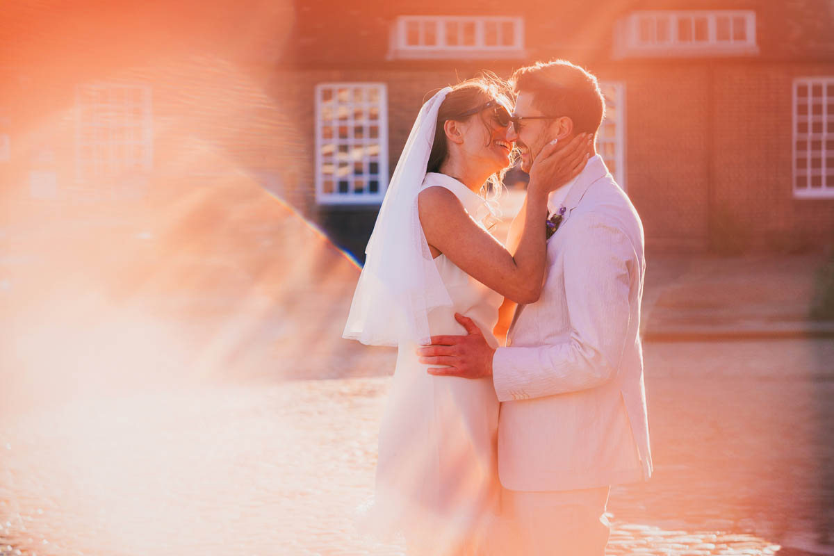 a bride kisses her husband at golden hour as sun flare hits the camera lens