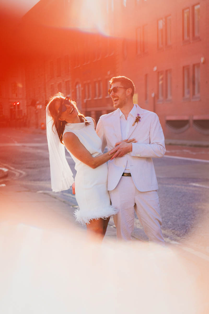 newly-weds laugh at the camera as evening sunlight hits the camera lens, causing flare