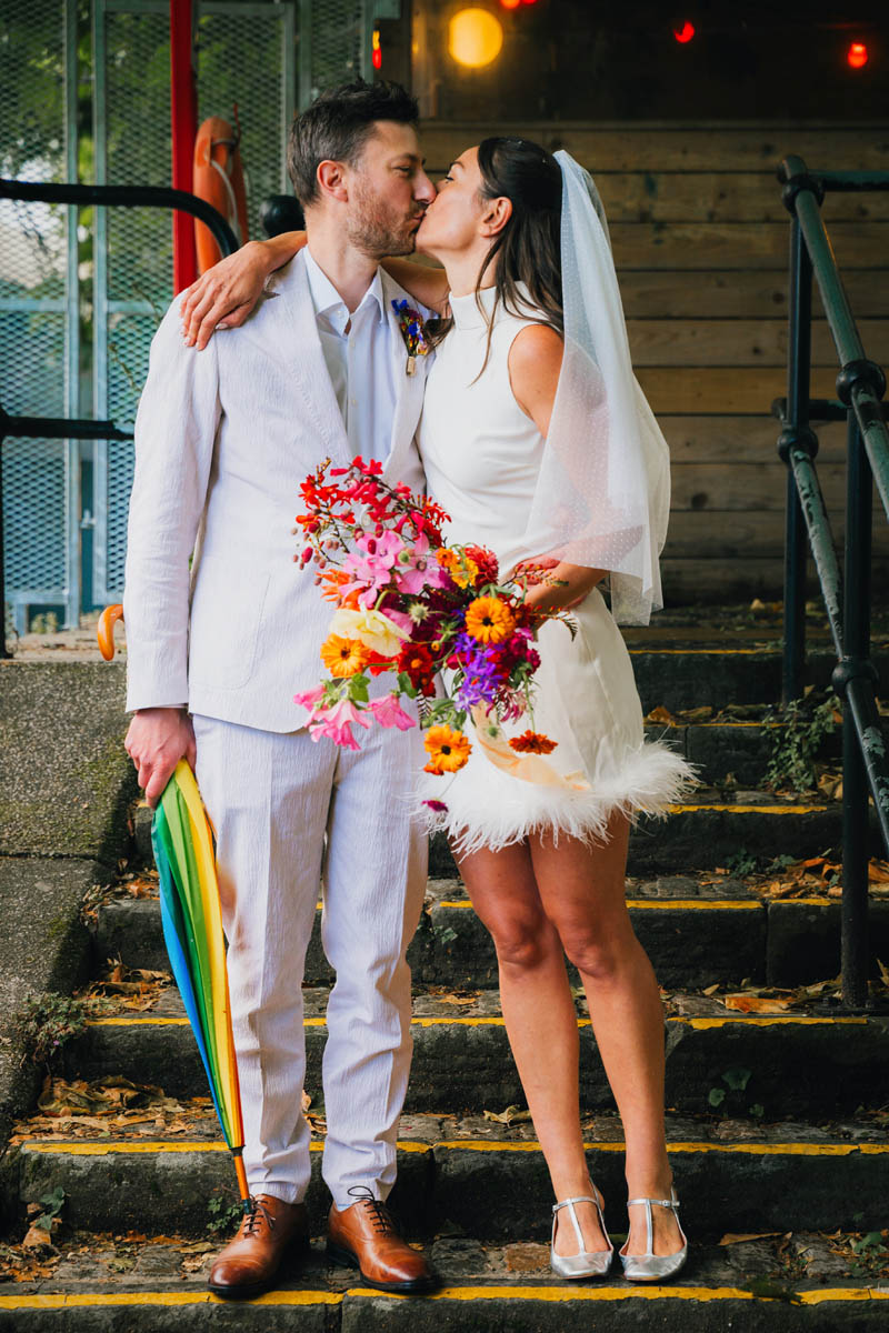 the bride kisses her groom is holds a rainbow umbrella