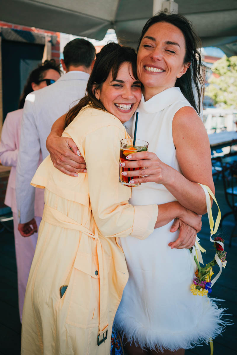 the bride hugs her bridesmaid as she drinks a pimms