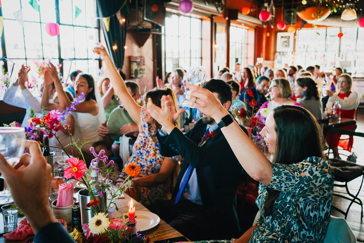 wedding guests raise their arms to a toast during the wedding speeches