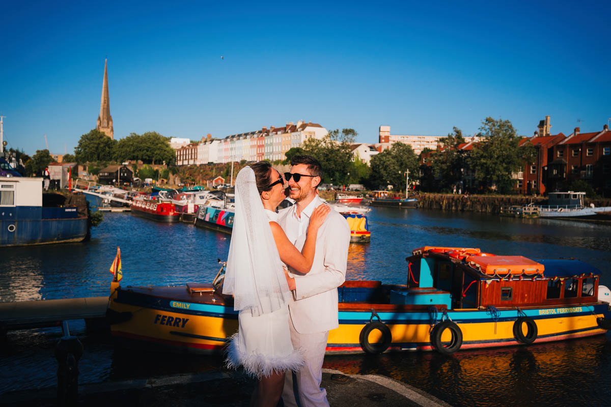 the bride and groom laugh in front of boats at Bristol Harbour