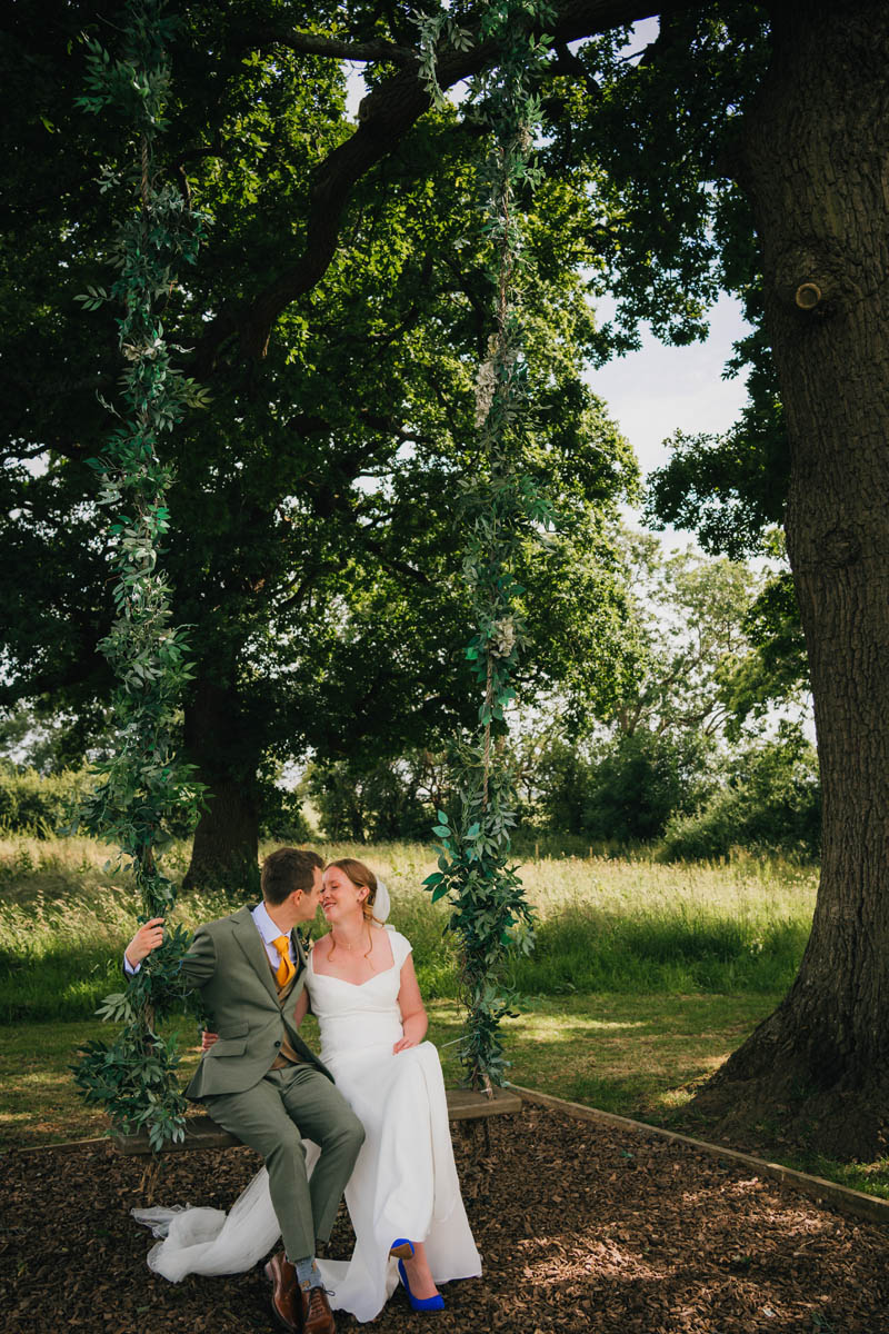 the groom kisses his new wife on the swing under a large tree