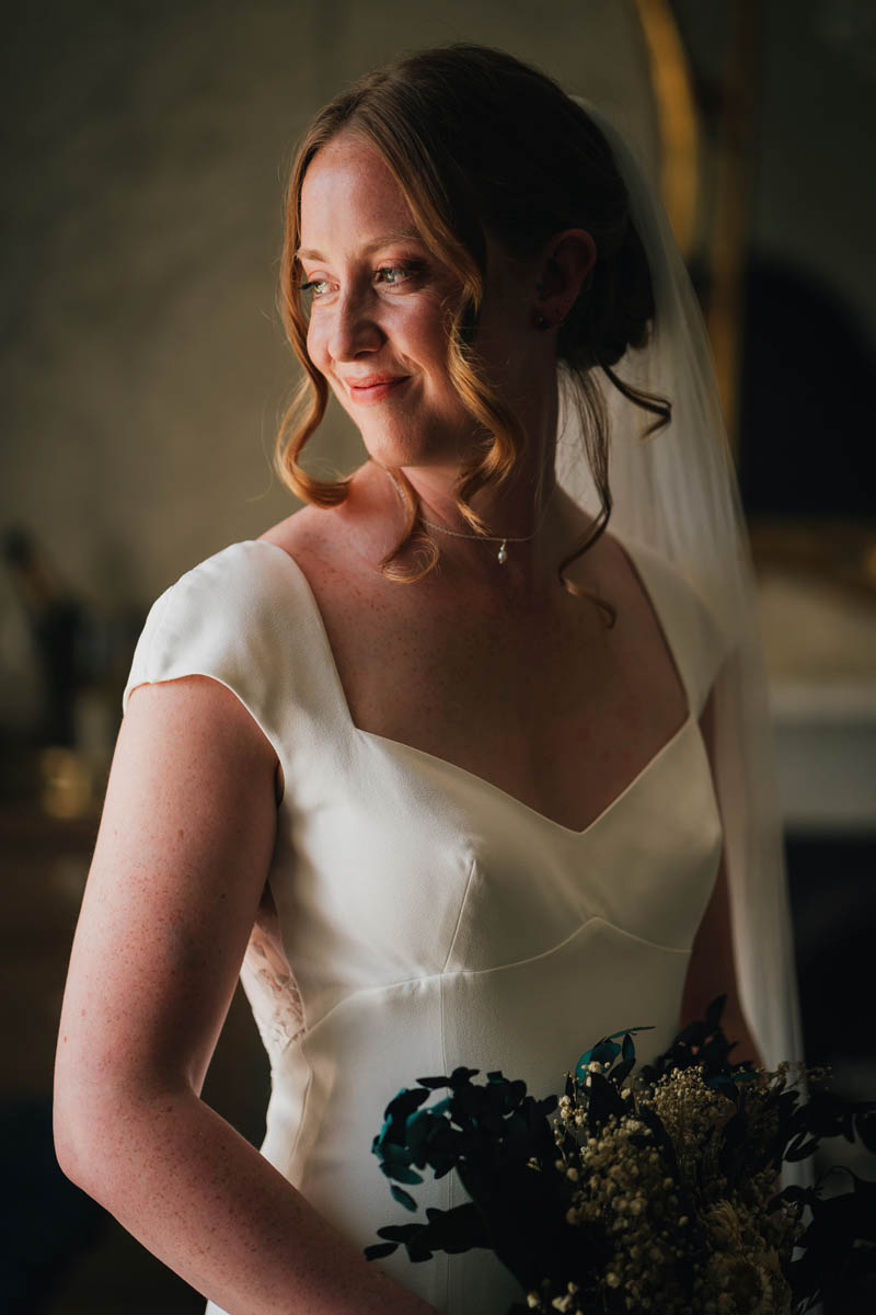 a bridal portrait of the bride in window light, she is holding her bouquet and wearing a wedding dress and veil.