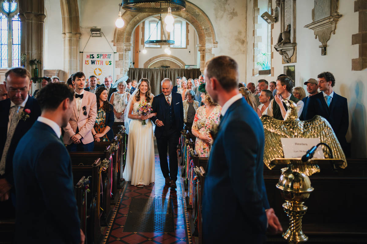 the bride is walked down the church aisle by her father as the groom and his best man wait for her arrival