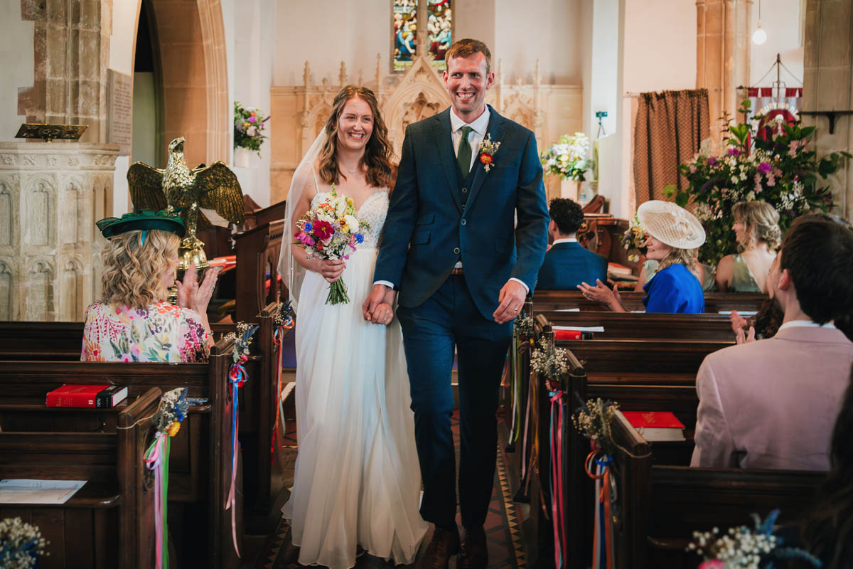 the newly-married man and wife walk up the aisle as wedding guests clap