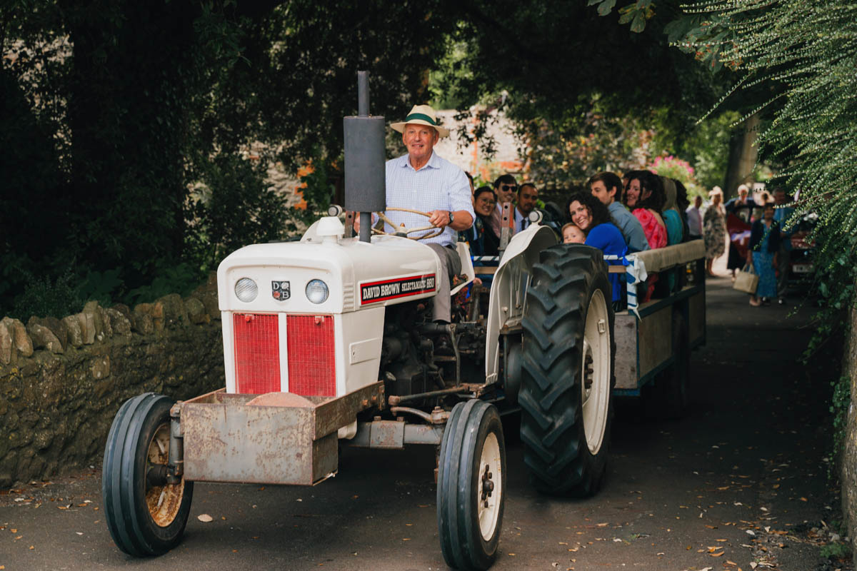 wedding guests are carted from the church to their cars in the back of a trailer pulled by an old fashioned tractor