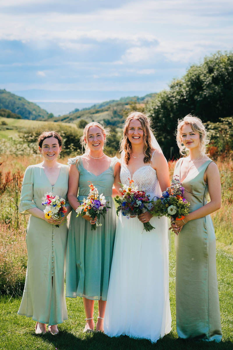 the bride and her bridesmaids in an assortment of green dresses holding their bouquets