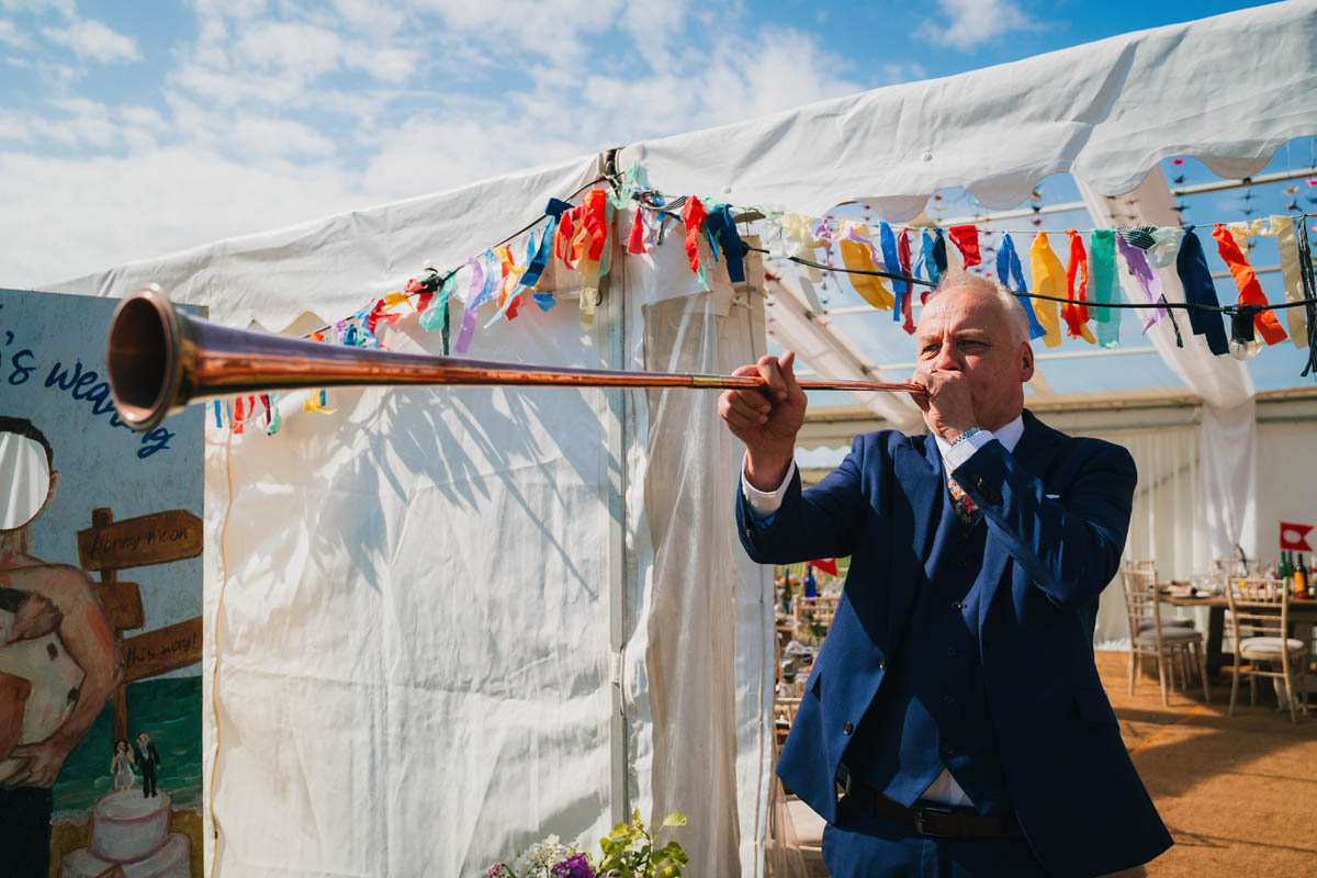 the father of the bride plays a large horn to signal the beginning of the wedding breakfast