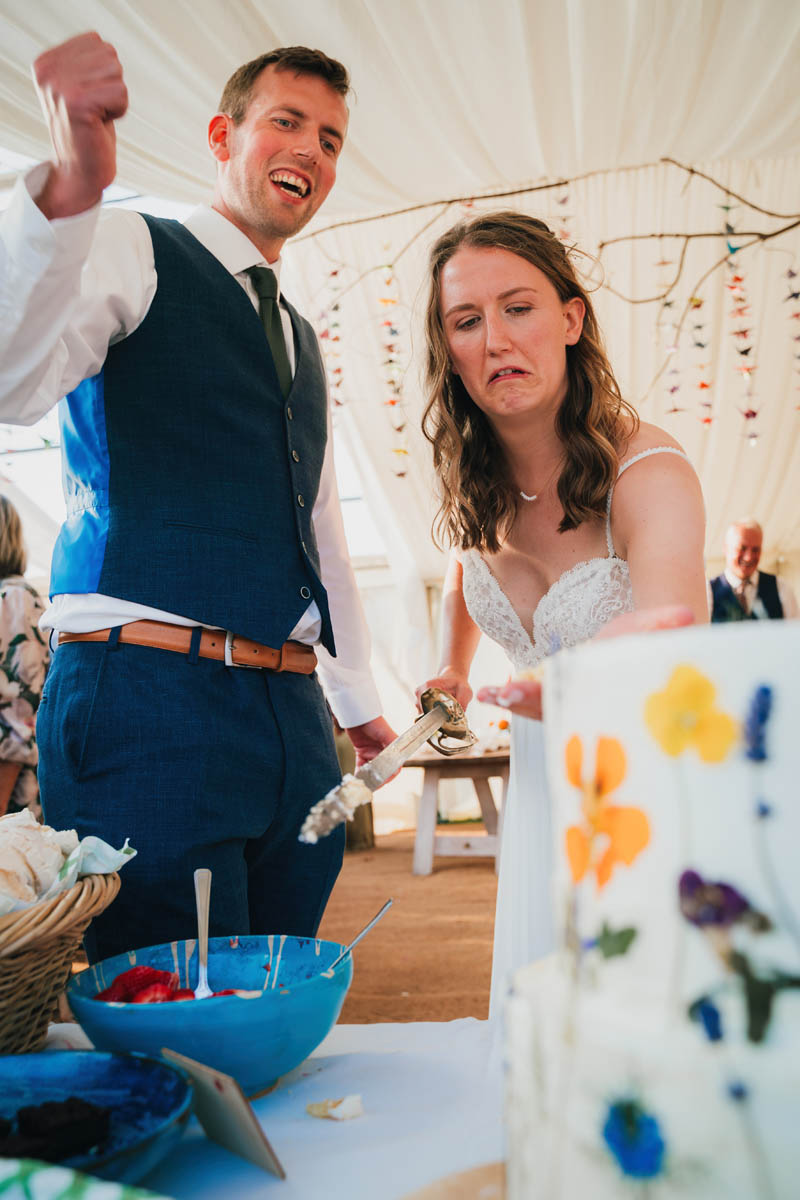 the bride and groom pull silly faces as they cut their two tiered wedding cake