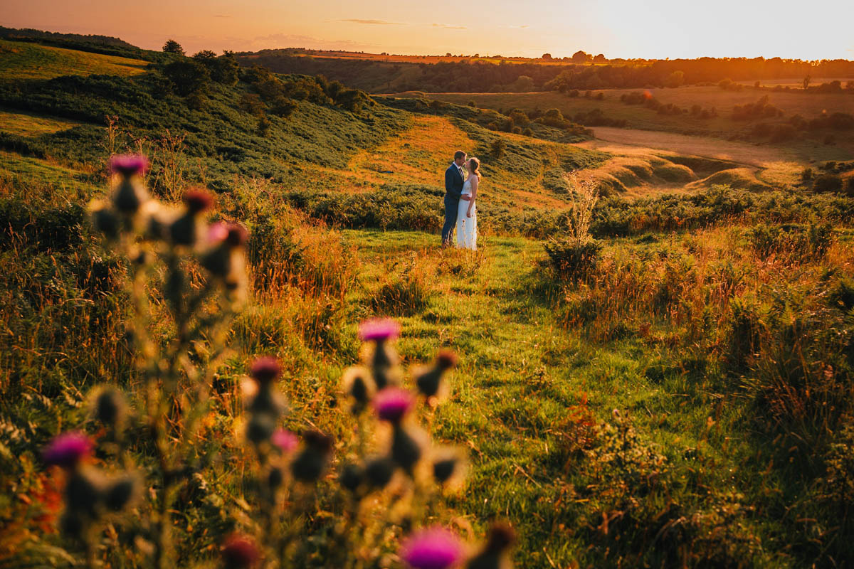 a landscape photograph of the Mendip Hills at golden hour featuring a bride and groom