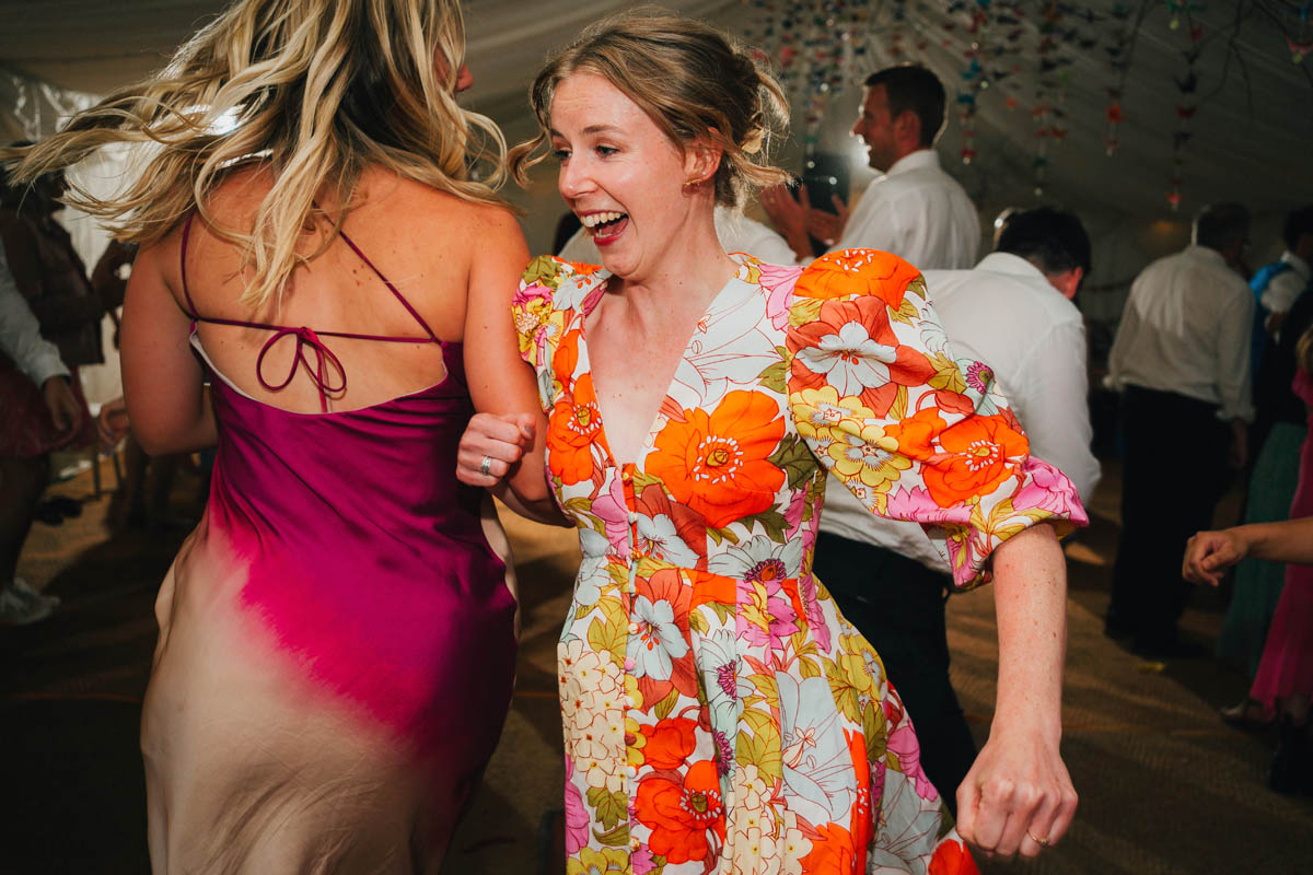 two women in bright orange and pink dresses spin one another around in a ceilidh