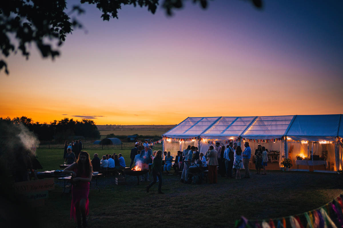 warren farm wedding venue at night, wedding guests gather around fire pits as the sun sets