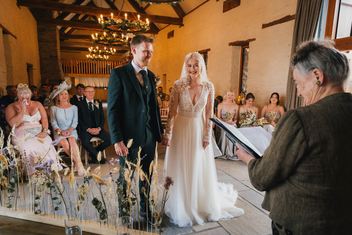 the bird and groom smile at the registrar who delivers the wedding ceremony, wedding guests look emotional in seats behind