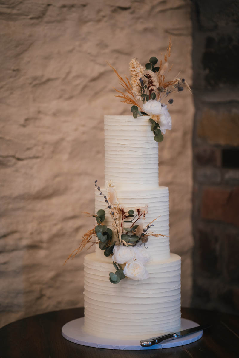 a three tiered ivory wedding cake with dried flower decorations