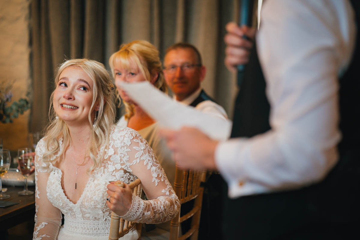 a bride looks emotional as her new husband delivers his speech