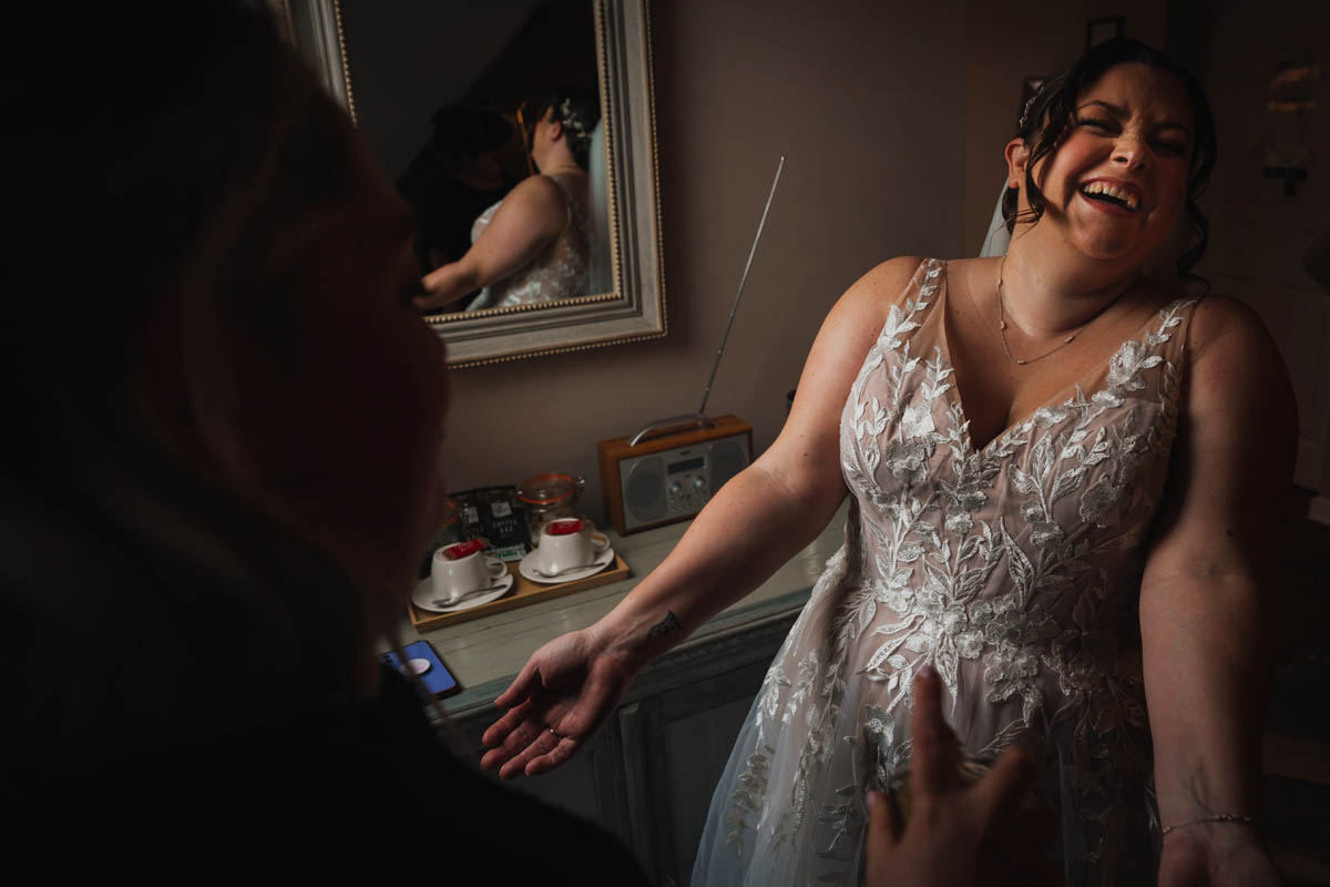 a bride throws her head back and laughs as as make up artist spays perfume