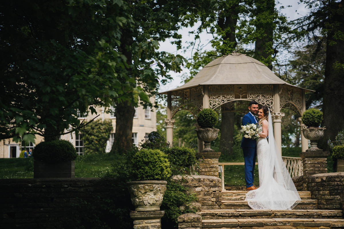 a couple stand next to a gazebo in a wedding dress and suit