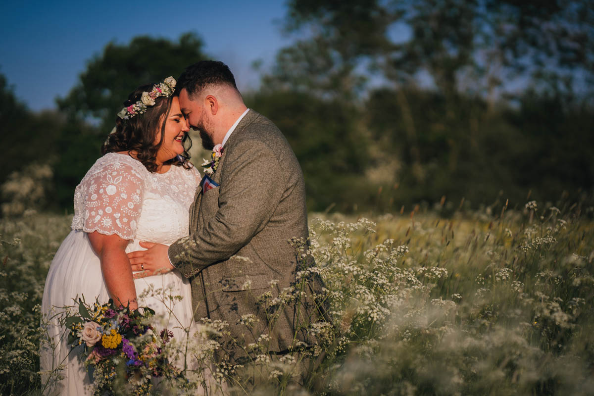 a couple stand in a field of cow parsley smiling on their wedding day