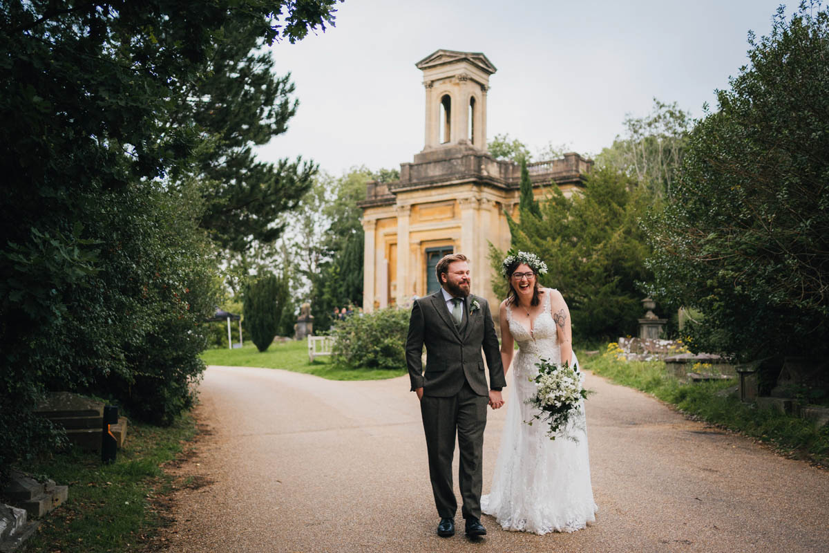 a husband and wife walk down a road witha. chapel behind them